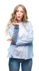 Beautiful young blonde woman over isolated background looking at the camera blowing a kiss with hand on air being lovely and sexy. Love expression.