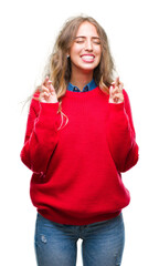 Beautiful young blonde woman wearing winter sweater over isolated background smiling crossing...