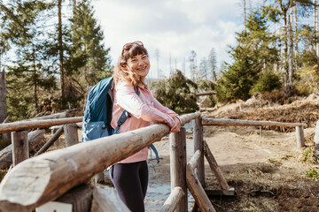 A young girl with a hiking backpack on her back leaned on the railing and is resting. Walking in the forest, hiking and a sporty lifestyle
