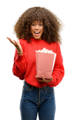 African american woman eating popcorn very happy and excited, winner expression celebrating victory...