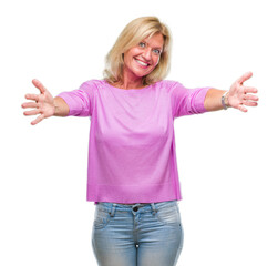 Fototapeta premium Middle age blonde woman over isolated background looking at the camera smiling with open arms for hug. Cheerful expression embracing happiness.