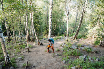 A man climbs a mountain on a rocky trail, climbing to the top, a young guy is a tourist with a backpack in the forest, trekking alone.