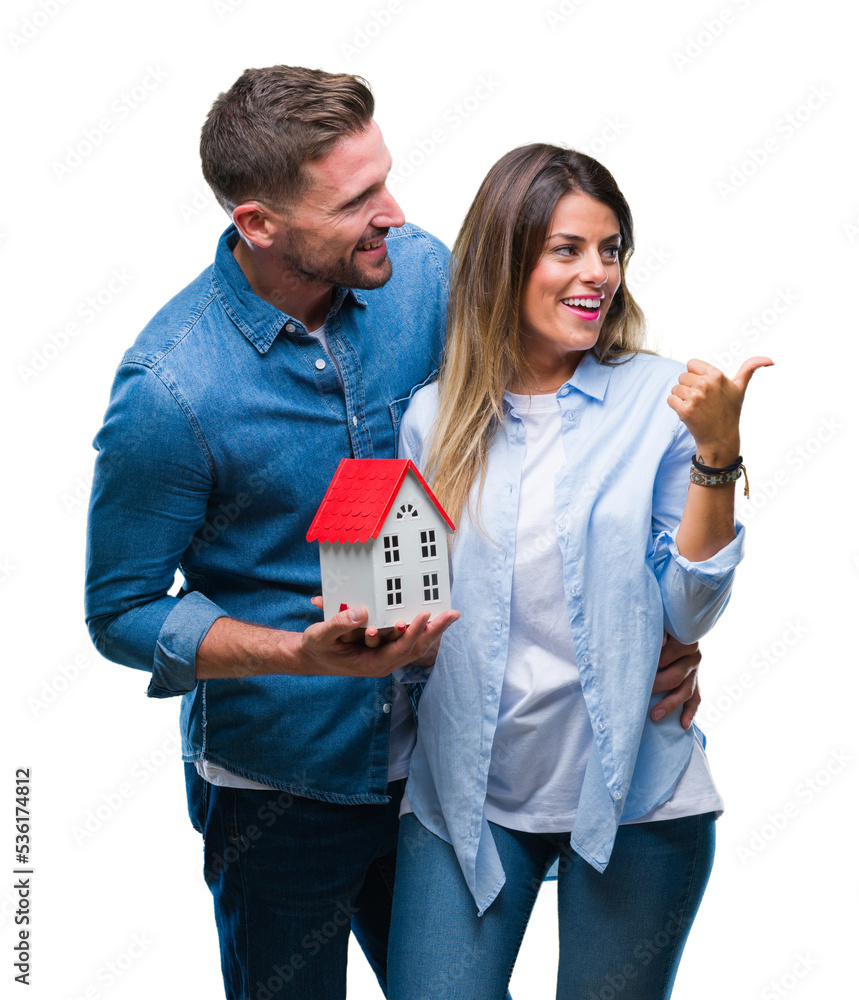 Poster young couple in love holding house over isolated background pointing and showing with thumb up to th