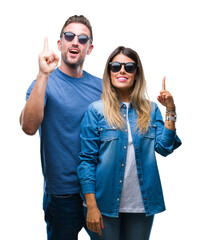 Young couple in love wearing sunglasses over isolated background pointing finger up with successful idea. Exited and happy. Number one.