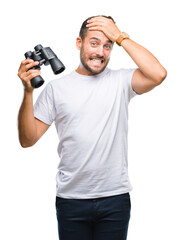 Young handsome man looking through binoculars over isolated background stressed with hand on head, shocked with shame and surprise face, angry and frustrated. Fear and upset for mistake.