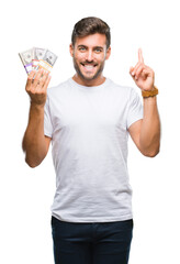 Young handsome man holding stack of dollars over isolated background surprised with an idea or question pointing finger with happy face, number one