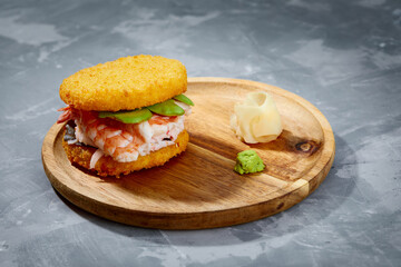 Pan-Asian cuisine concept. Japanese sushi burger made from rice bread, crab meat, avokado and wasabi sauce. Serving on wooden board. copy space
