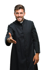 Young catholic christian priest man over isolated background smiling friendly offering handshake as greeting and welcoming. Successful business.