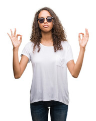 Young hispanic woman wearing sunglasses relax and smiling with eyes closed doing meditation gesture with fingers. Yoga concept.