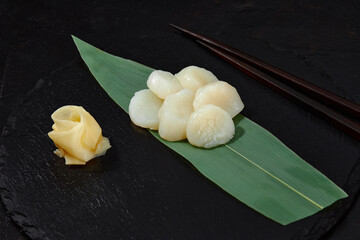 Fresh octopus sashimi on bamboo leaf on black.
