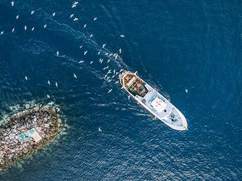 Top view of a fishing trawler coming back to the port and the seagulls are flying over it.
