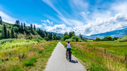Fototapeta na wymiar Woman on an e-bike on the trail along the Okangen River Canal between Oliver and Osoyoos in the Okanagen Valley of British Columbia, Canada
