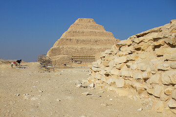Pyramid of Saqqara, known as Pyramid of Steps, wall of ruins and horses in the background in...