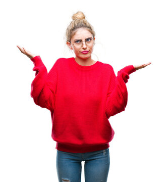 Young beautiful blonde woman wearing red sweater and glasses over isolated background clueless and confused expression with arms and hands raised. Doubt concept.
