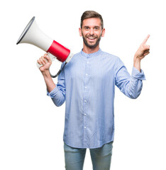 Young handsome man yelling through megaphone over isolated background very happy pointing with hand and finger to the side