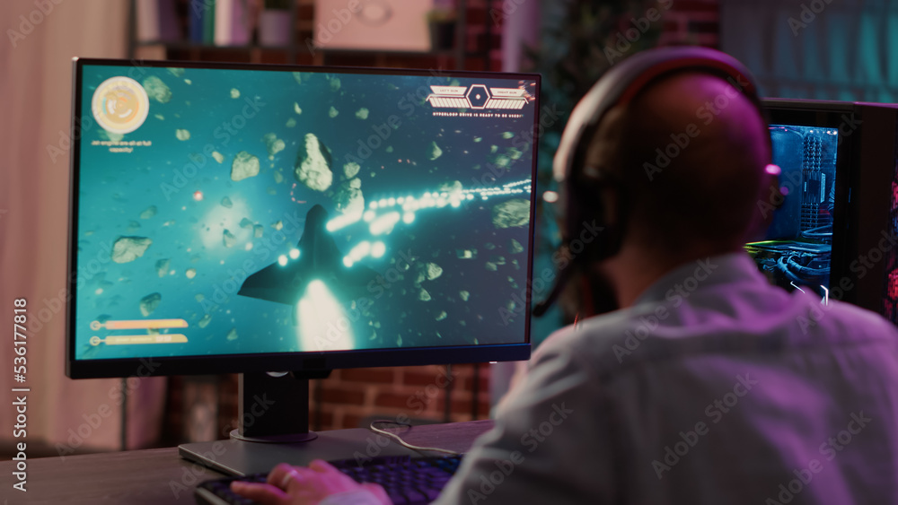 Poster over shoulder view of gamer streaming fast paced space shooter action game on gaming pc. man playing