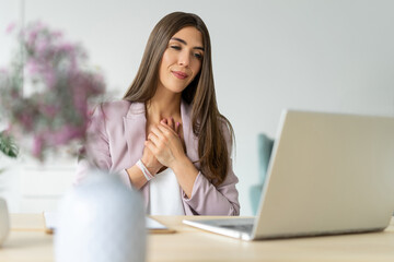 Young female psychologist in pink jacket conducts an online appointment. Supports his client and expresses understanding of problem through video call on work laptop. Minimalistic light office.