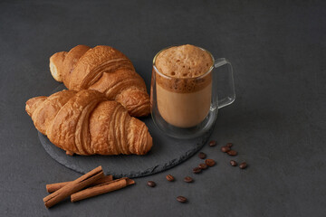 Croissants with cinnamon and coffee on a dark stone table. French breakfast. Composition for advertising and menus of cafes and restaurants