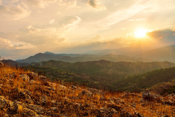 beautiful highland landscape with amazing view from a top with golden grass and green bushes to a canyon with majectic mountains and scenic cloudy sunset on background