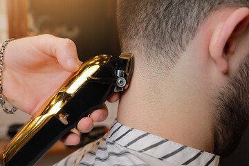 Hairdresser, barber cutting the hair from the back of the client's head with a gold electric clipper, razor. Man visiting hairstylist in barbershop.Barber is trimming client hair. Beauty salon