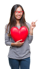 Young asian woman in love holding read heart over isolated background very happy pointing with hand and finger to the side