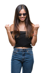 Young asian woman wearing sunglasses over isolated background very happy and excited doing winner gesture with arms raised, smiling and screaming for success. Celebration concept.