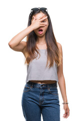 Fototapeta premium Young asian woman wearing sunglasses over isolated background peeking in shock covering face and eyes with hand, looking through fingers with embarrassed expression.