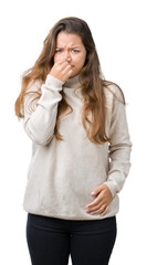 Young beautiful brunette woman wearing turtleneck sweater over isolated background smelling...