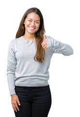 Obraz premium Young beautiful brunette woman wearing sweater over isolated background doing happy thumbs up gesture with hand. Approving expression looking at the camera with showing success.