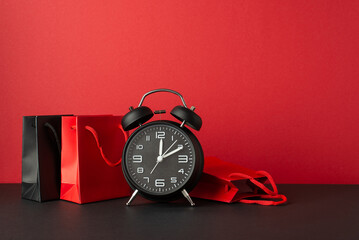 Cyber monday concept. Photo of alarm clock red and black paper bags on black tabletop red wall...