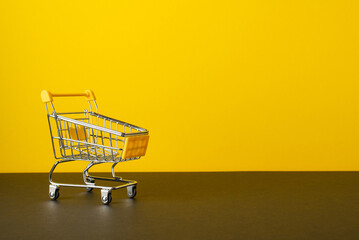 Black friday sales concept. Photo of shopping cart on tabletop yellow wall background with copyspace