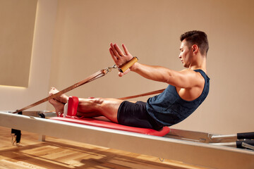 Fit man doing a lunge stretch yoga pilates exercise to strengthen and tone his muscles using a reformer in gym. Health and fitness concept