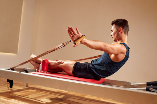 Fit Man Doing A Lunge Stretch Yoga Pilates Exercise To Strengthen And Tone His Muscles Using A Reformer In Gym. Health And Fitness Concept