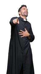 Young Christian priest over isolated background Laughing of you, pointing to the camera with finger...
