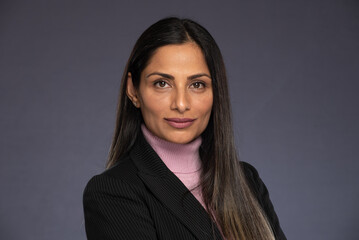 Studio headshots of beautiful Asian Indian woman in business attire on gray background. 