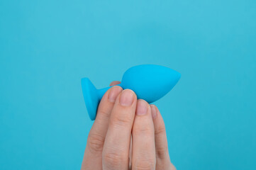 Woman holding a blue anal plug on a blue background. 