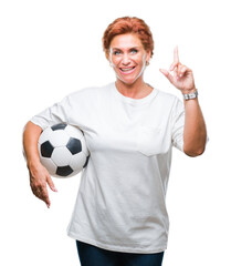 Atrractive senior caucasian redhead woman holding soccer ball over isolated background surprised...