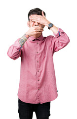Young handsome man wearing pink shirt over isolated background Covering eyes and mouth with hands, surprised and shocked. Hiding emotion