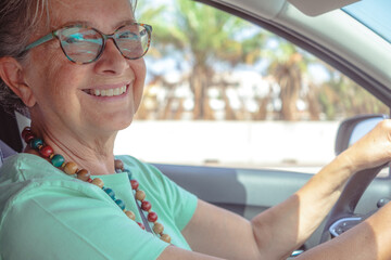 Happy caucasian senior woman driving the car smiling looking at camera