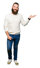 Young hipster man wearing winter sweater smiling cheerful presenting and pointing with palm of hand looking at the camera.