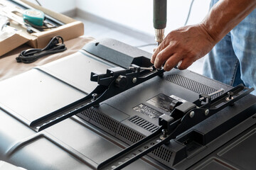 man installing the wall base for the television, it is a smart tv, adjusting with screwdriver