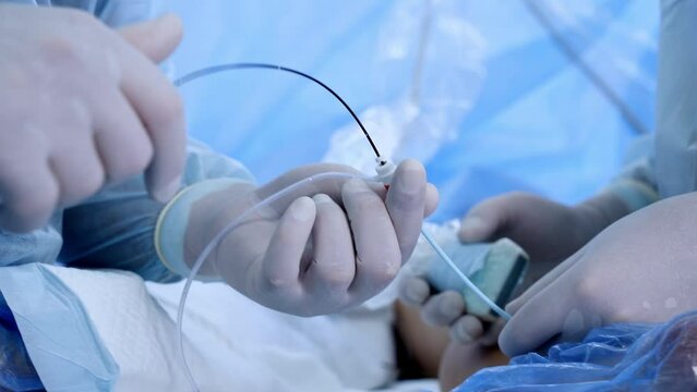 Male gloved hands holding and using the surgical tools and devices. Close up. Vascular operation in process.