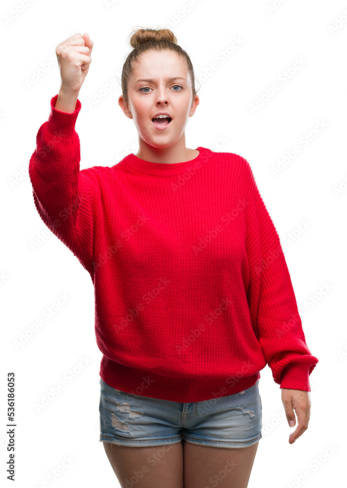 Wall mural young blonde woman wearing bun and red sweater angry and mad raising fist frustrated and furious whi