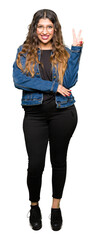 Obraz premium Young beautiful woman wearing glasses and denim jacket smiling with happy face winking at the camera doing victory sign. Number two.