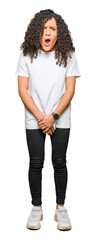 Fototapeta premium Young beautiful woman with curly hair wearing white t-shirt In shock face, looking skeptical and sarcastic, surprised with open mouth