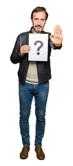 Handsome middle age man holding paper with question mark with open hand doing stop sign with serious and confident expression, defense gesture