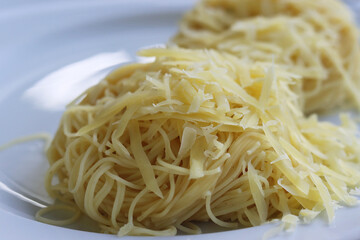 Rolled Spaghetti noodles with shredded Parmesan cheese on the white plate. Side view. Cooked spaghetti in grey glass plate isolated on white background. Close-up.