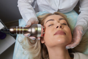 A cosmetologist in rubber gloves does the rf-lifting procedure on the face. In the background, the...