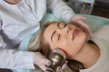 A cosmetologist in rubber gloves does the rf-lifting procedure on the face. In the background, the...