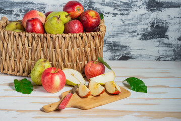 Basket with a harvest of fresh pears and apples on a white table. Sliced pears and apples on a cutting board. Space for text